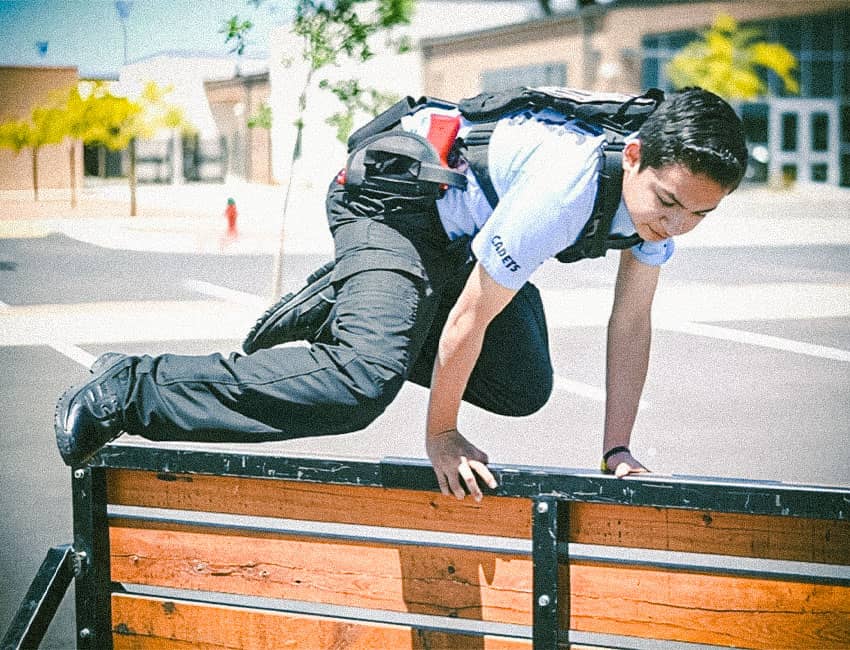 Young girl in police cadet gear jumping over railing.