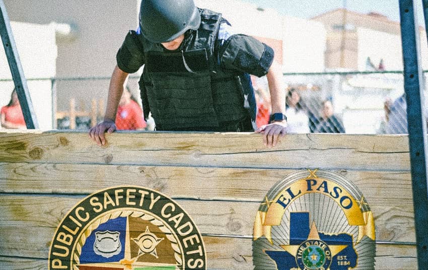 A young man wearing police gear jumping over wall.